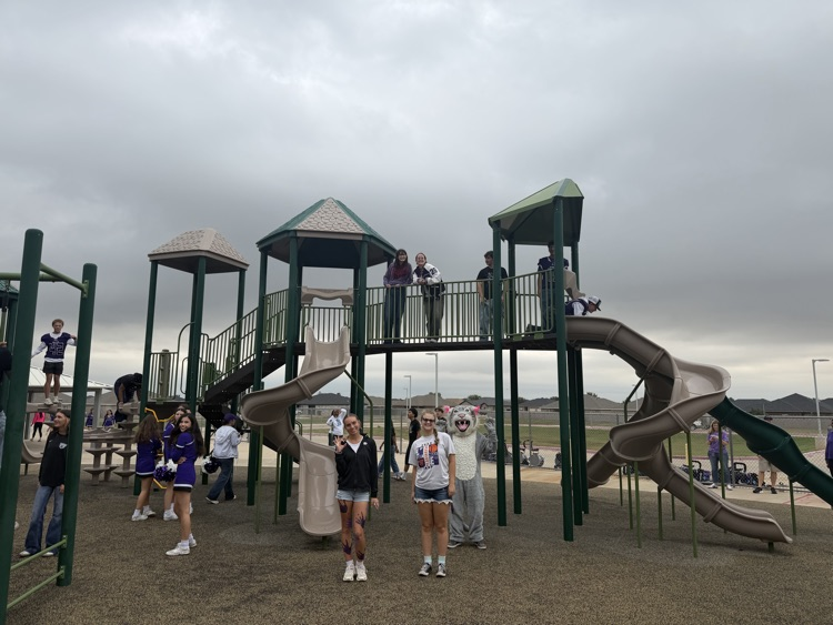 Group of people in athletic gear at a playground. Some on slides, others standing. Overcast sky.
