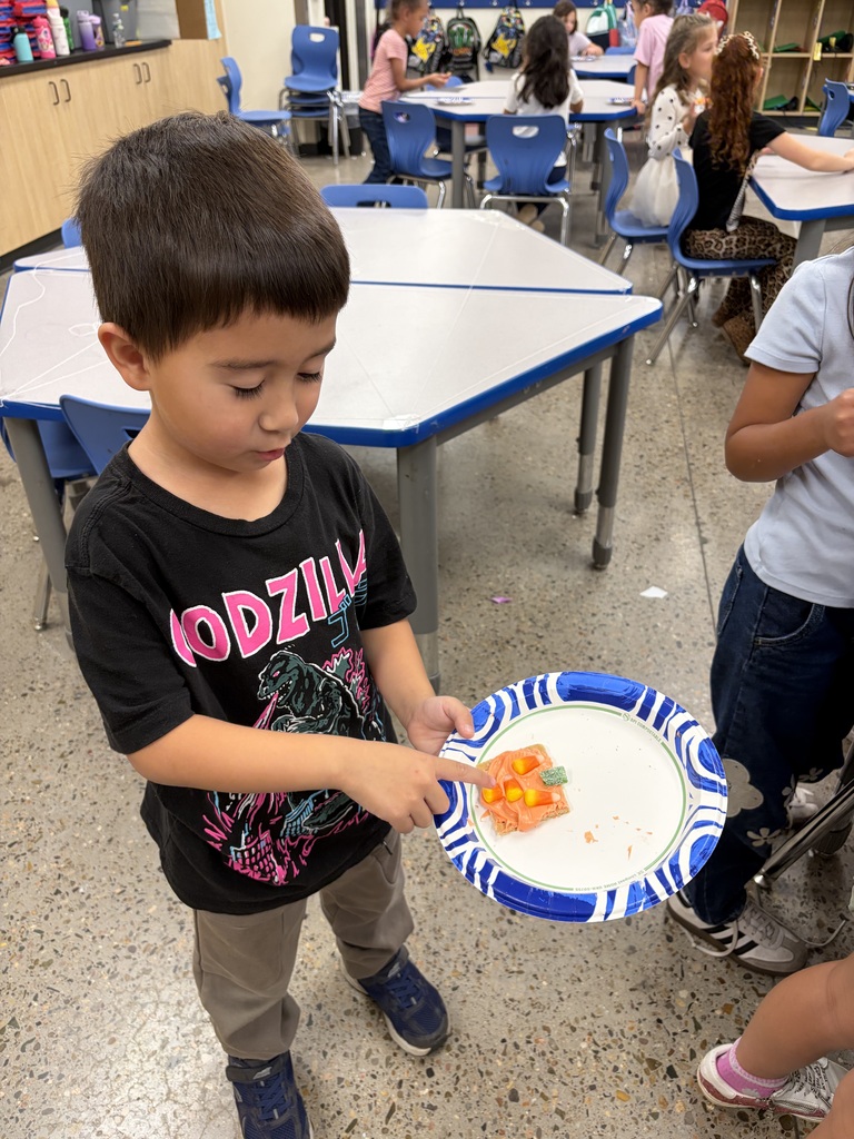 A young boy is holding a plate with a small piece of food in a classroom.