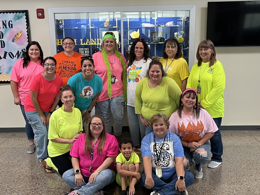 Adult staff and one student pose with vibrant neon clothing and accessories on.