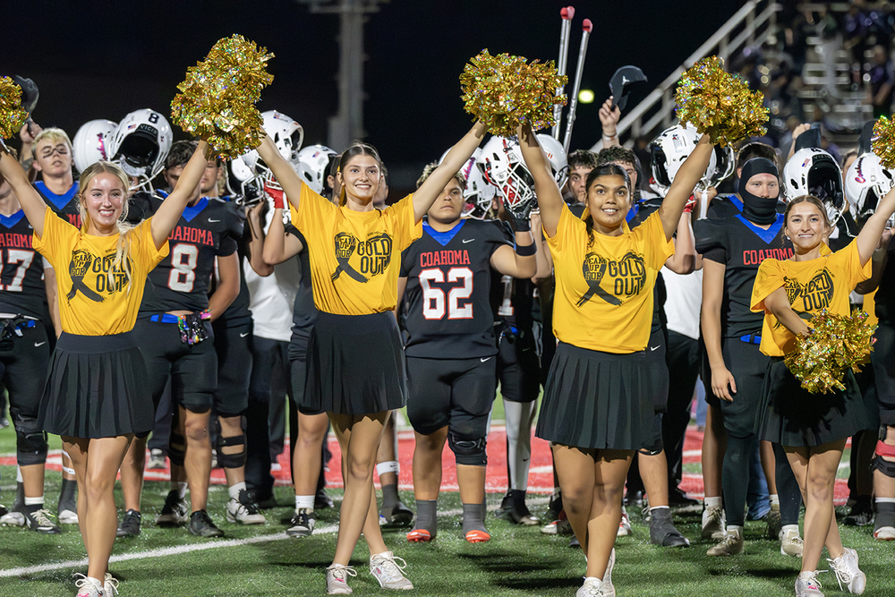 Cheerleaders raising their pom poms in the air after a football game