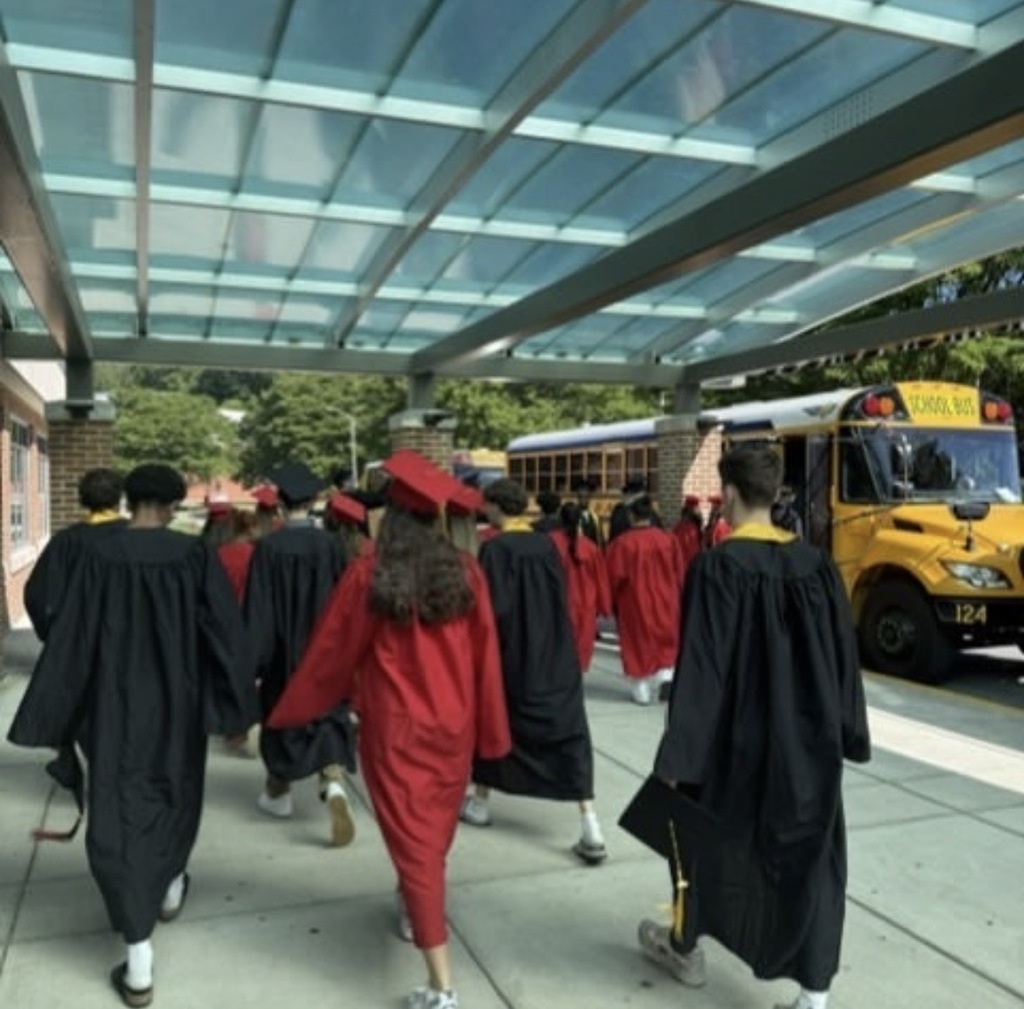 graduates with cap and gown walk along the sidewalk