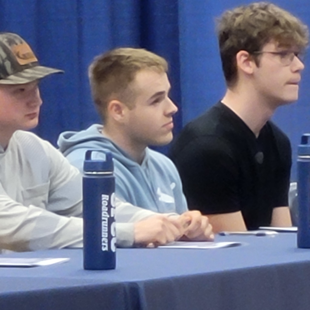Three boys sitting at table at State Fair Community College signing day.