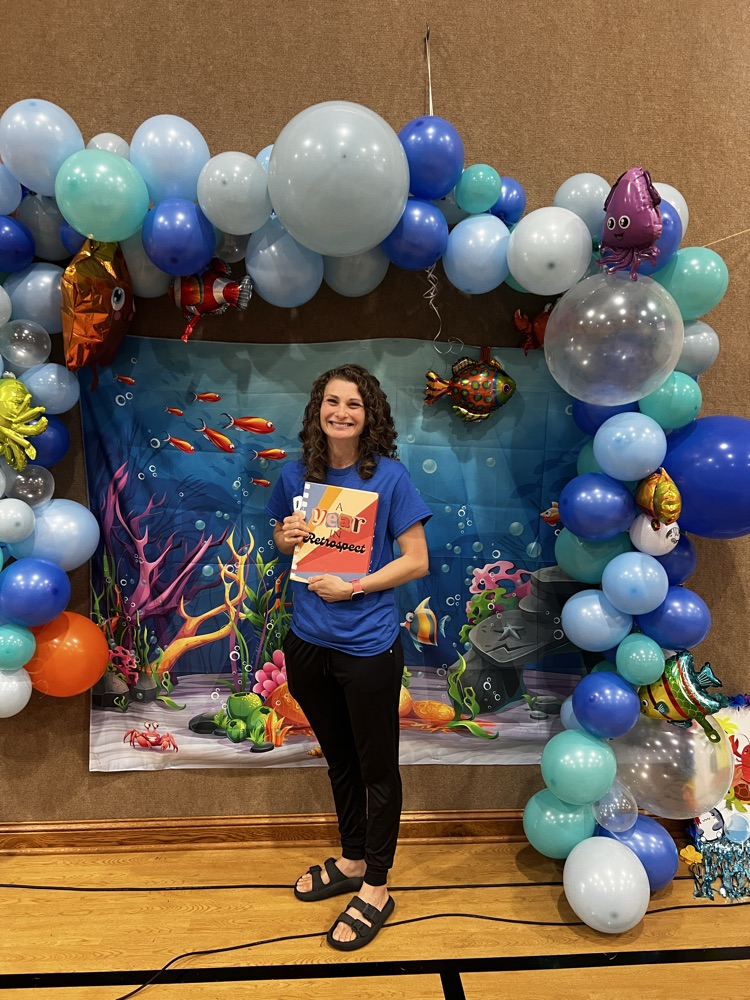 Mrs. Schnakenberg stands holding the yearbook that was dedicated to her titled “A Year in Retrospect”.