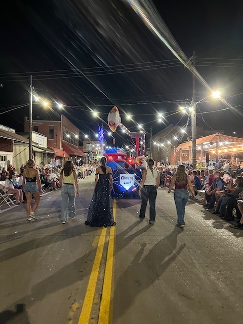 Senior class members walk behind the float during the parade on Highway 52. Chairs are lined up on both sides of the parade route with spectators. 