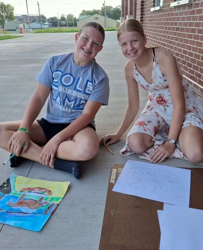 Students Aliana Camirand and Jody Dixon pause a moment from drawing and painting to pose for a photograph.