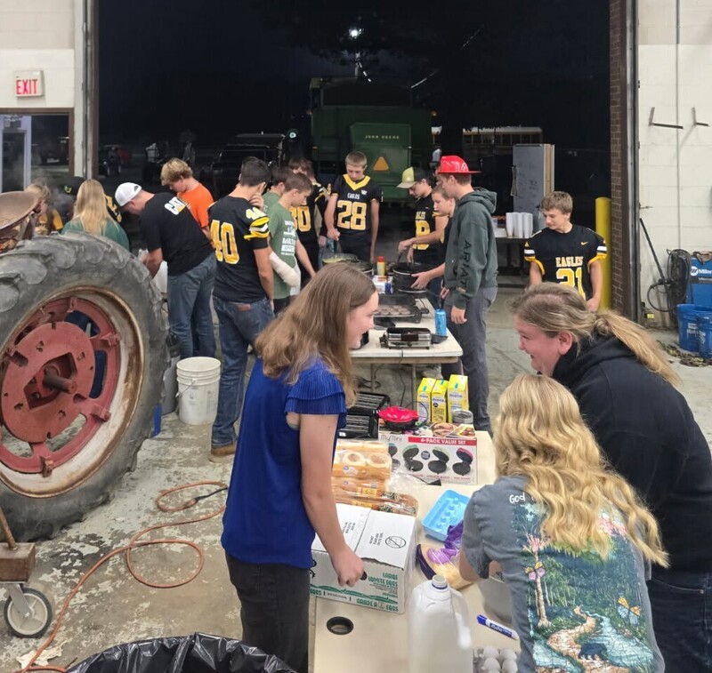 Colonel Crawford students and staff prepare breakfast together in the school’s agricultural shop. Students, including several wearing black-and-gold Eagles football jerseys, gather around tables with griddles, cooking supplies, eggs, milk, and other breakfast ingredients.