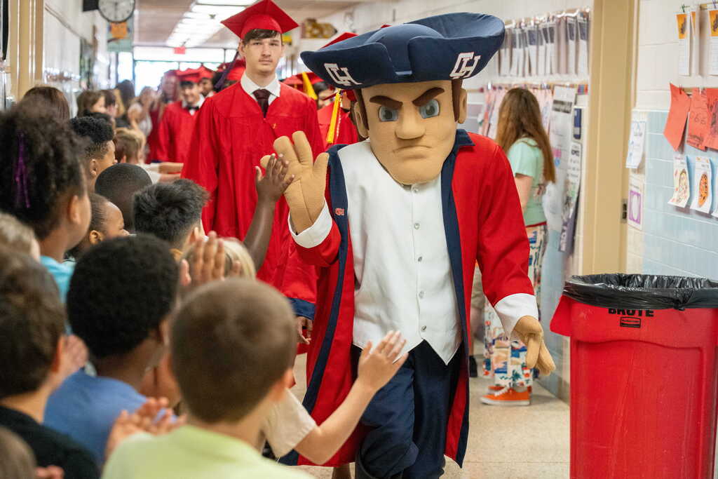 Colonial Man leading parade of graduates and high fiving the elementary students