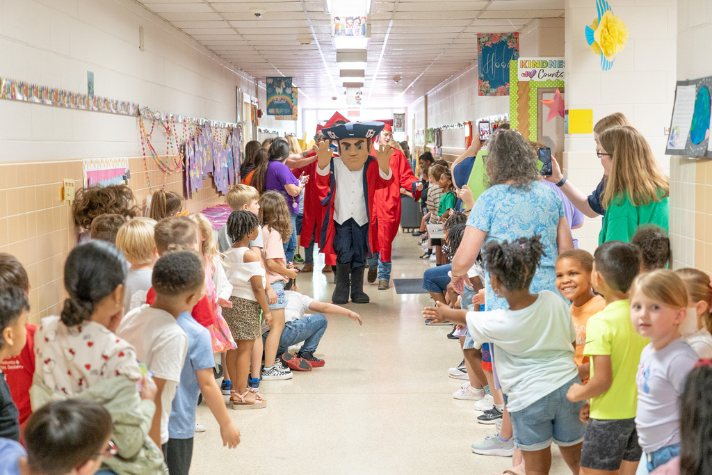 Colonial Man Walking down elementary school hallway waving to children