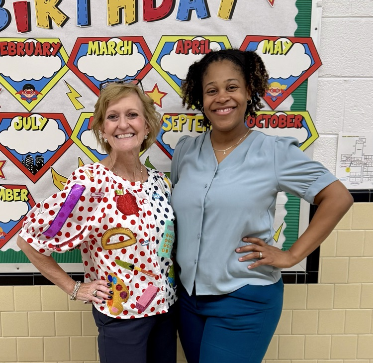 North Elementary Principal and Assistant Principal pose smiling in front of a superhero-themed bulletin board in a school hallway.