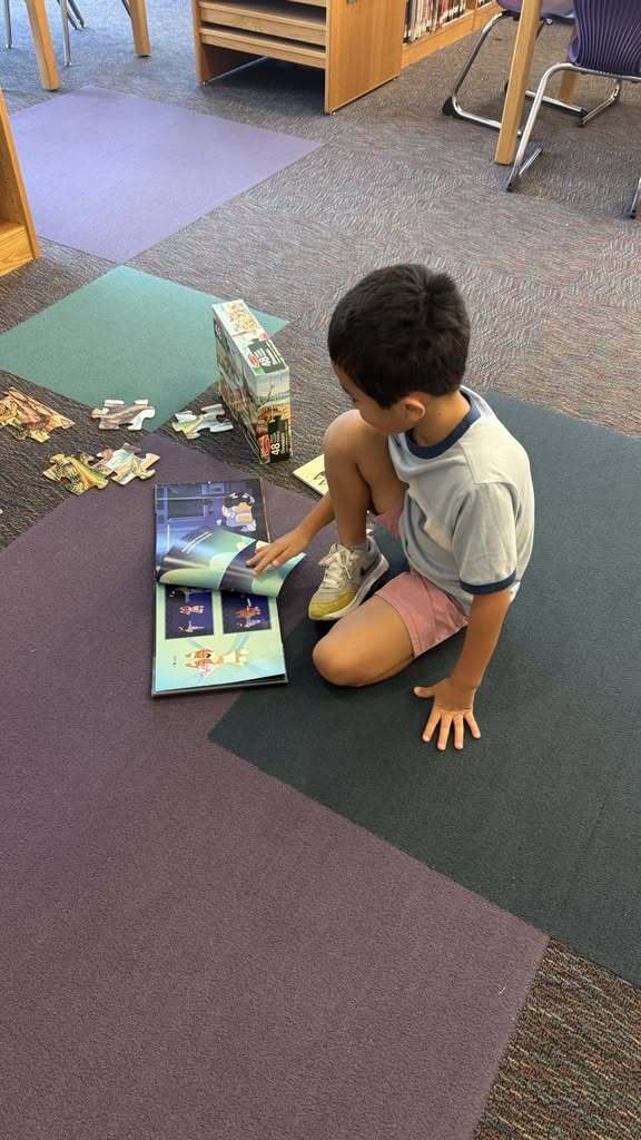 Student looking at book and doing a puzzle on the floor