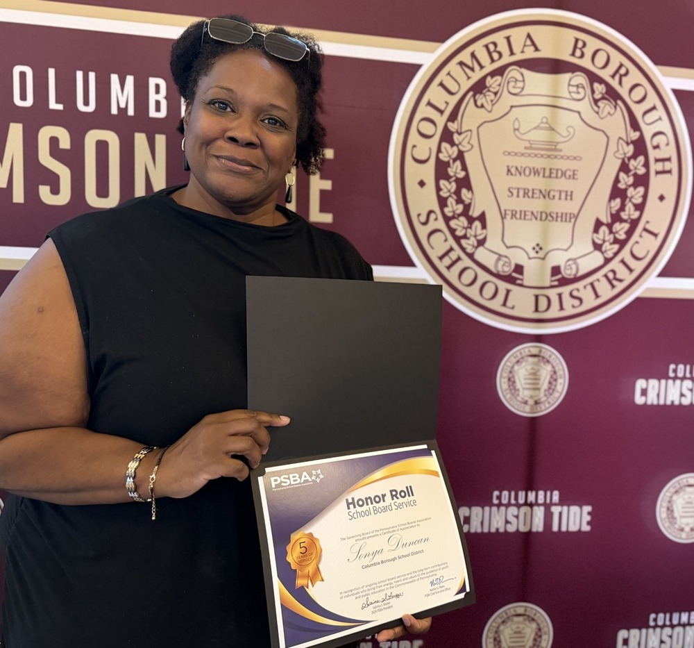 Rev. Sonya Duncan holds a Pennsylvania School Boards Association Honor Roll certificate recognizing her five years of service on the Columbia Borough School District Board of Directors, standing in front of a Columbia Crimson Tide backdrop.