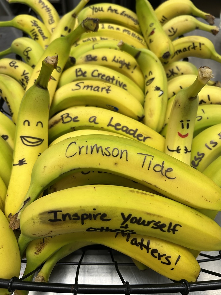 A close-up view of bananas in a basket with handwritten motivational messages and doodled faces. Visible phrases include “Crimson Tide,” “Be a leader,” and “Inspire yourself and others!” The bananas are arranged together as an uplifting display with encouraging affirmations.