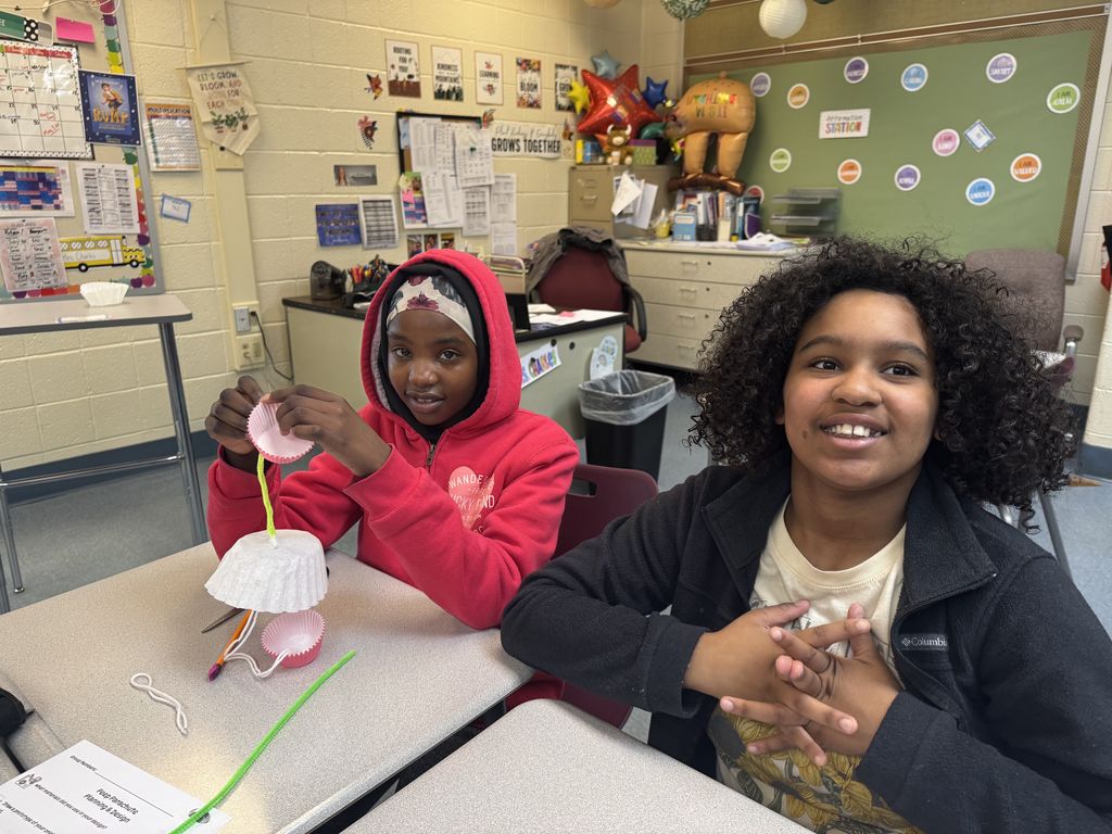 2 students sitting at desks working on parachute
