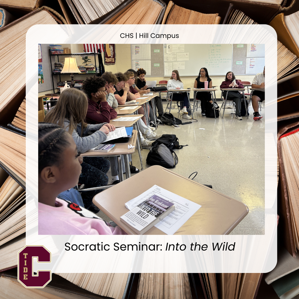 A high school classroom where a diverse group of students sit in a circle of desks participating in a Socratic seminar discussion. Each student has papers and a copy of Into the Wild on their desk, and backpacks rest on the floor. A teacher’s desk with a lamp and bookshelves is visible in the background, along with a whiteboard displaying notes. Text overlay reads “CHS | Hill Campus” and “Socratic Seminar: Into the Wild,” with a school logo in the corner.