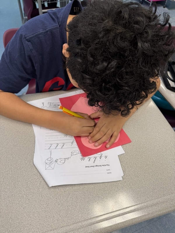 boy writing a kindness card on a heart shapped card