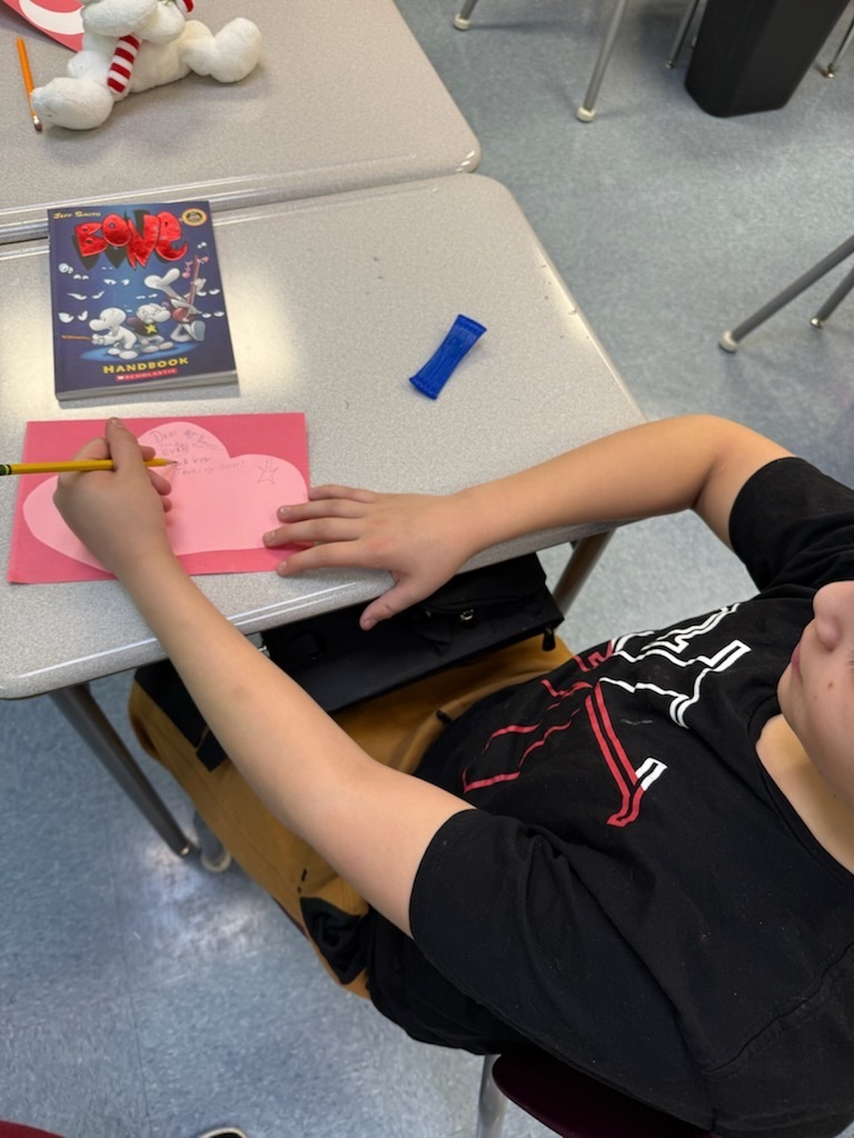 boy writing a kindness card on a heart shapped card