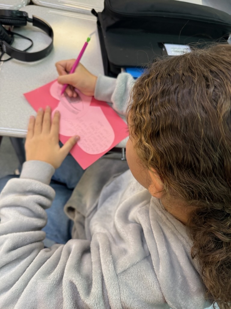 Girl writing a kindness card on a heart shapped card