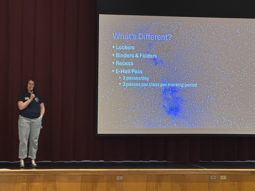 A teacher standing on stage speaking in front of students