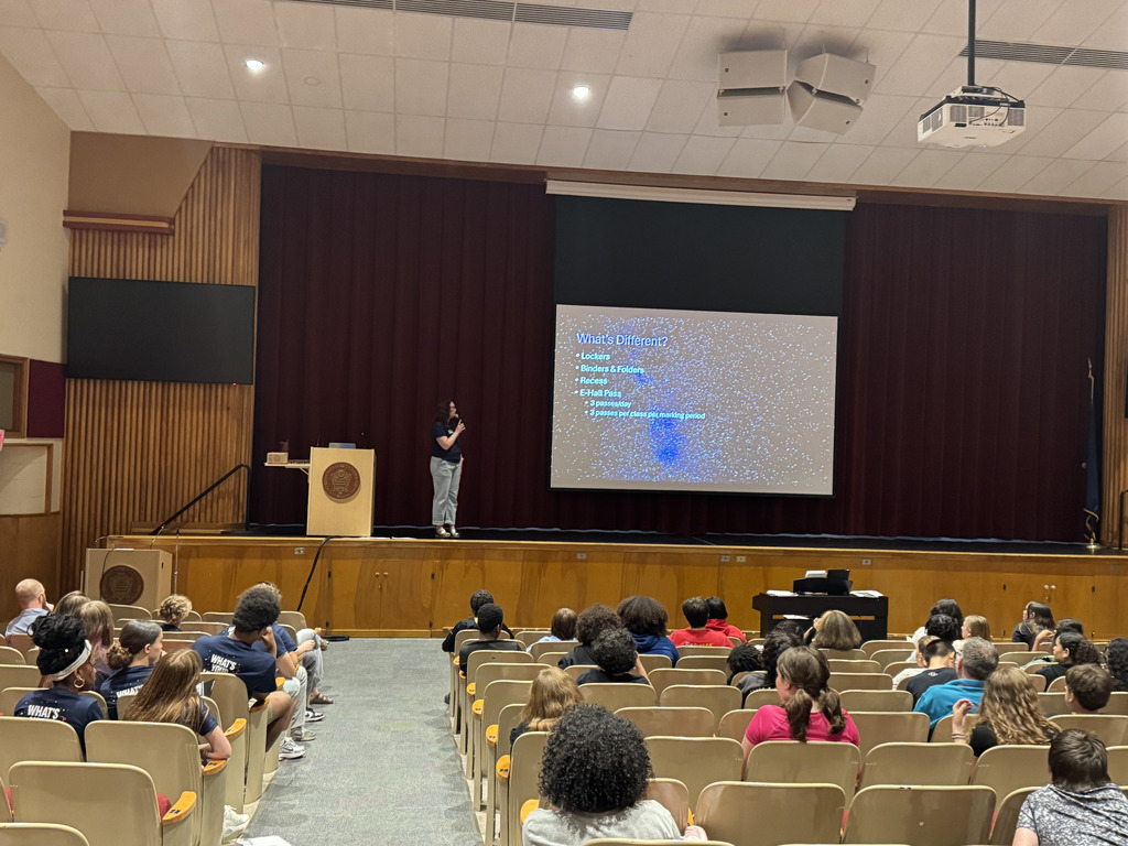 A teacher standing on stage speaking in front of students