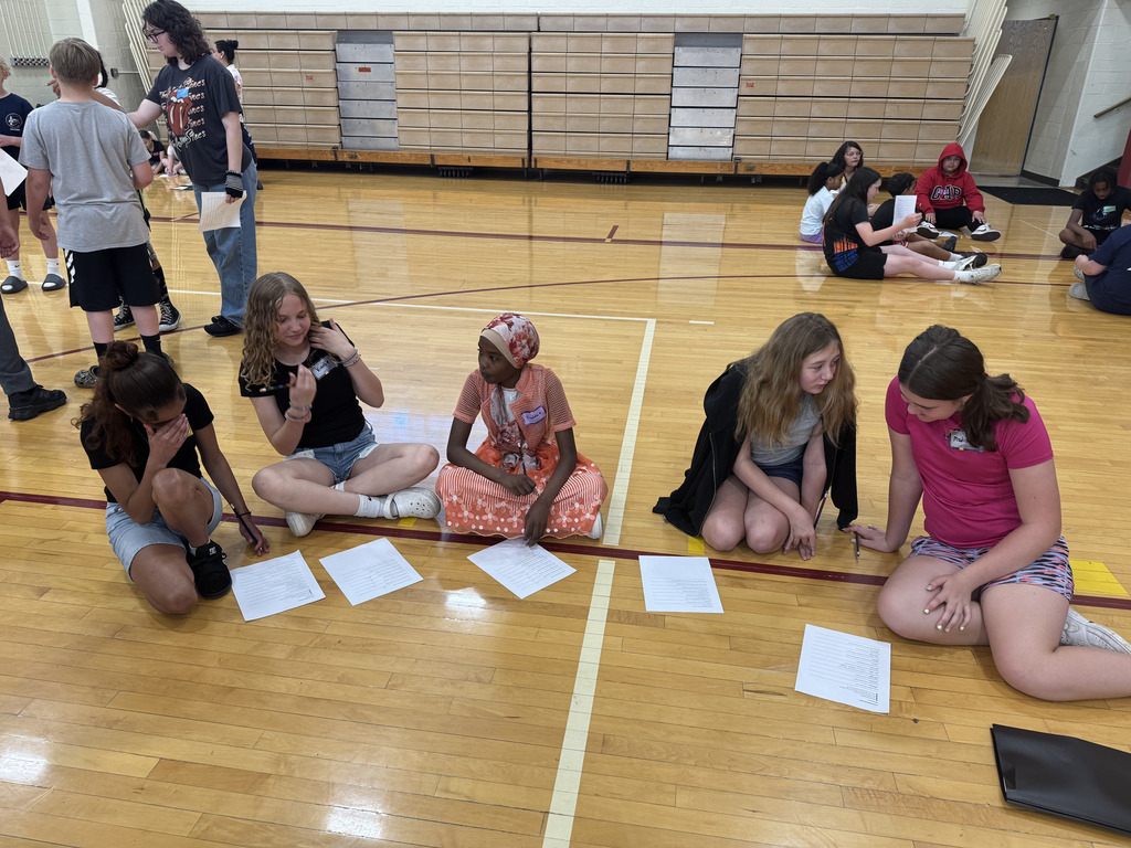 Students sitting on the floor of a gym with papers 