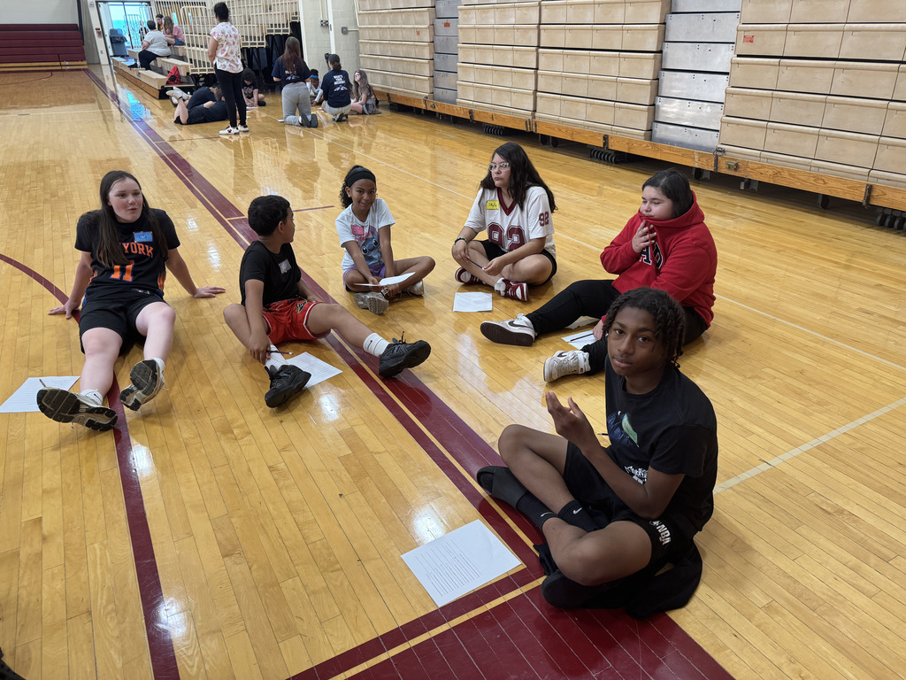 Students sitting on the floor of a gym with papers