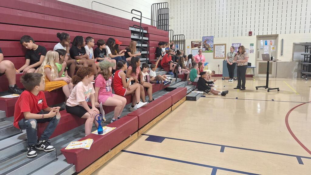 Students sitting on the bleachers listening to adults speaking