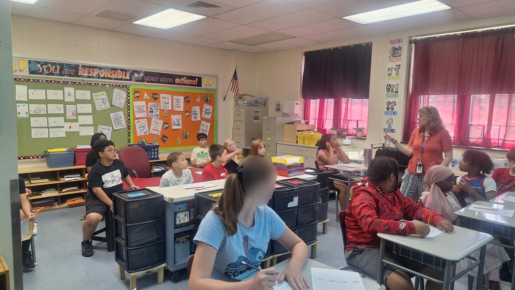 kids sitting in a classroom listening to a teacher talk