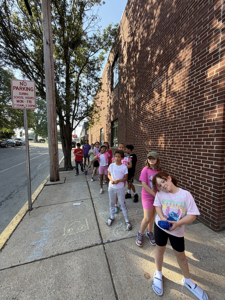 Students standing on the sidewalk outside a building with colorful chalk on the ground