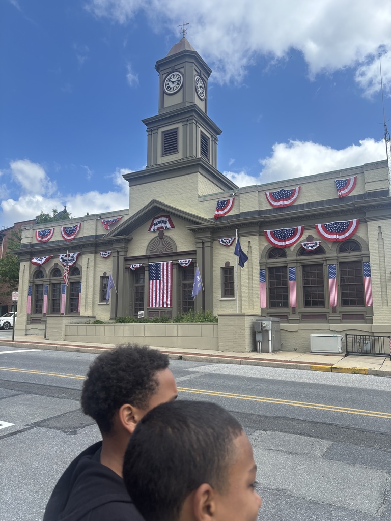Two young men are focused on a clock tower, discussing its features while standing in a lively urban setting.