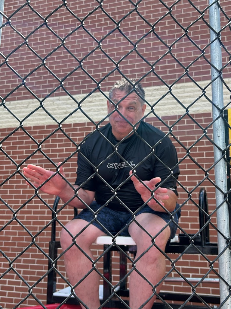 playfully while waiting to be dunked. The dunk tank is set up outdoors beside a brick school building.