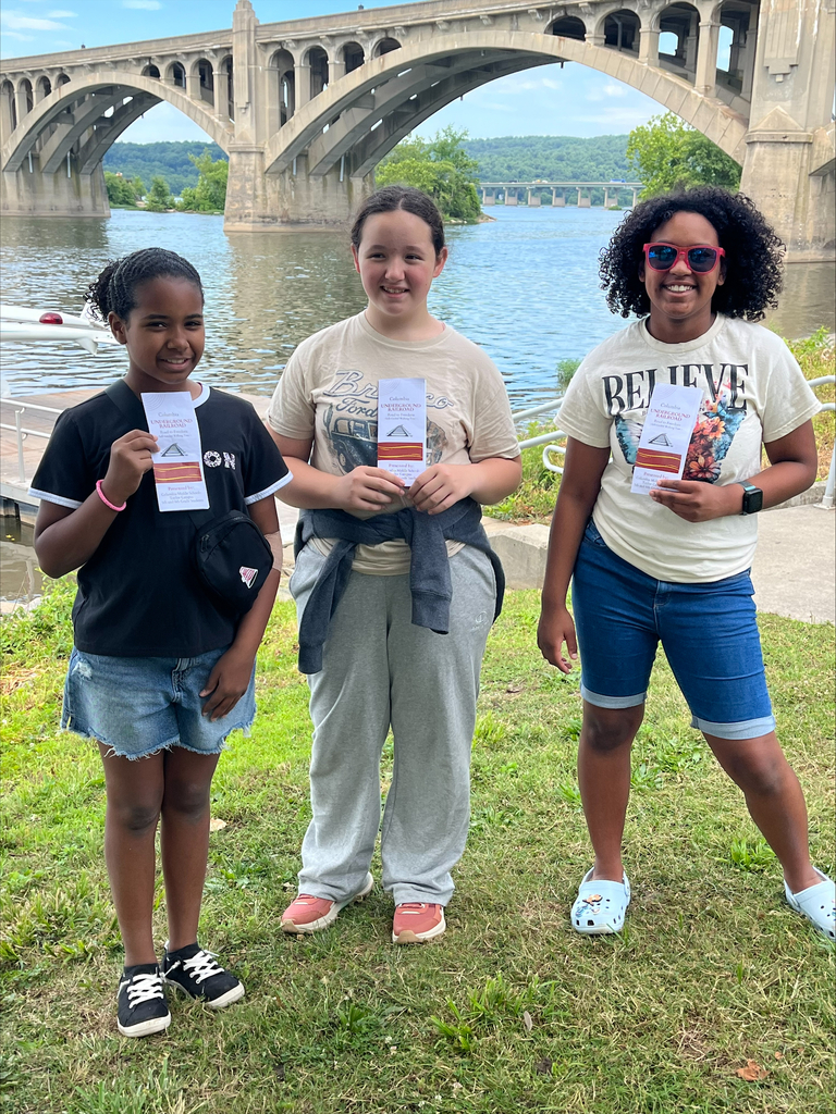 3 students standing outside smiling and holding a flyer