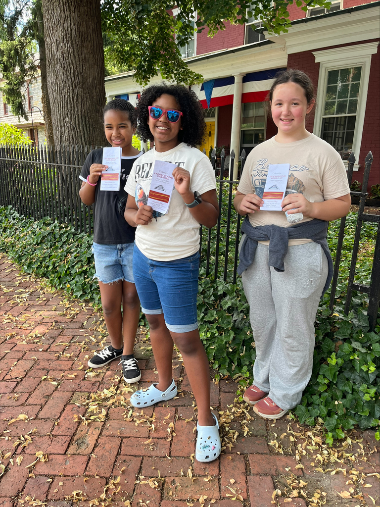 3 students standing outside smiling and holding a flyer
