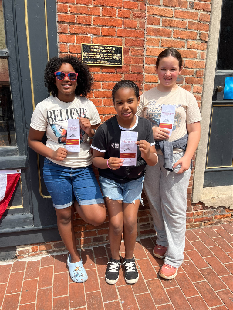 3 students standing outside smiling and holding a flyer
