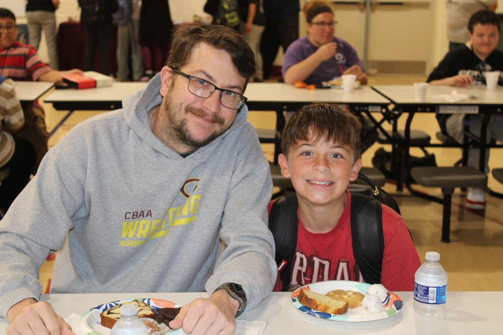 parent and student smiling together sitting at a table with breakfast