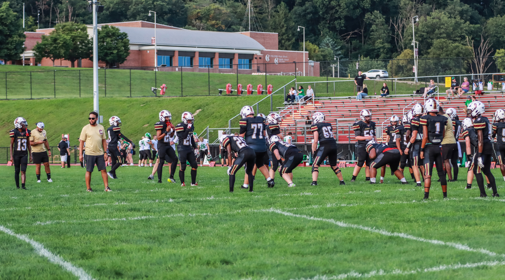 Columbia youth football players in black uniforms warm up on a field as coaches and spectators look on.