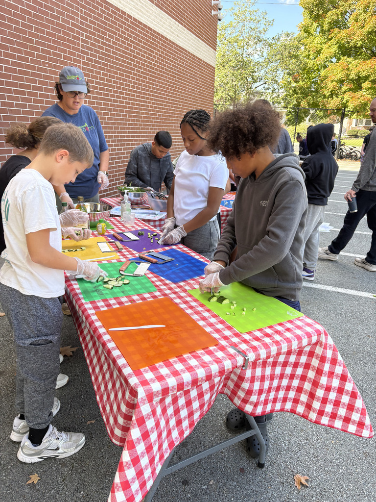 Students prepare vegetables on colorful cutting boards while working together at an outdoor food preparation station.