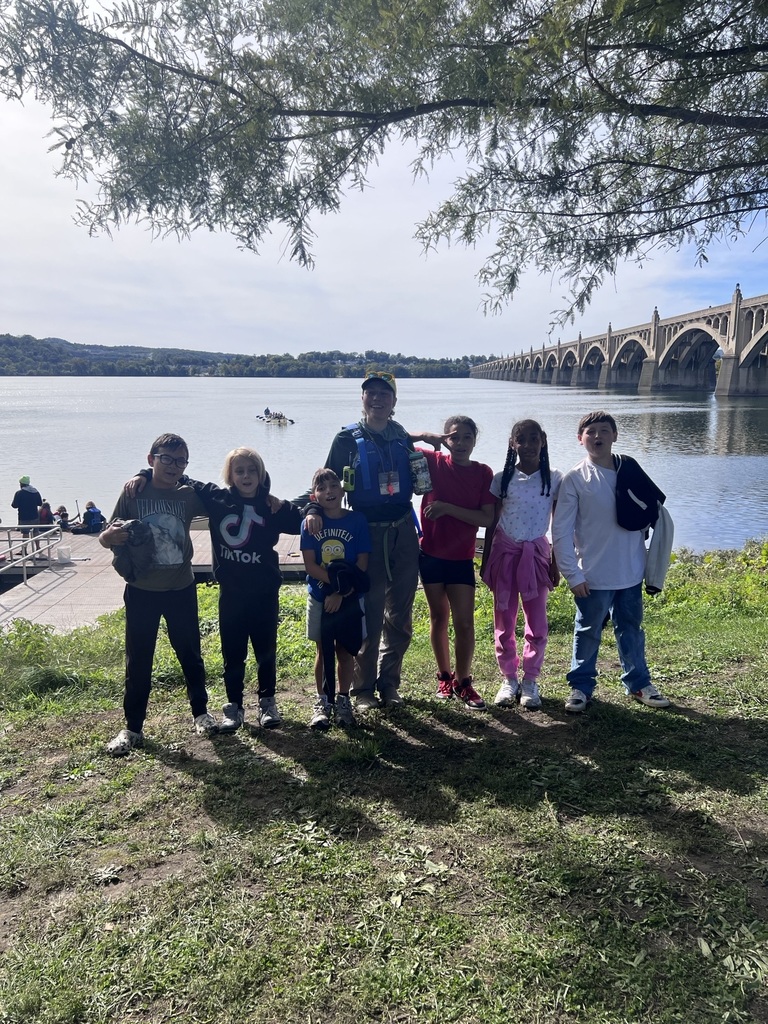 A group of students poses with an instructor beside the Susquehanna River, with the river and the arched bridge visible in the background.
