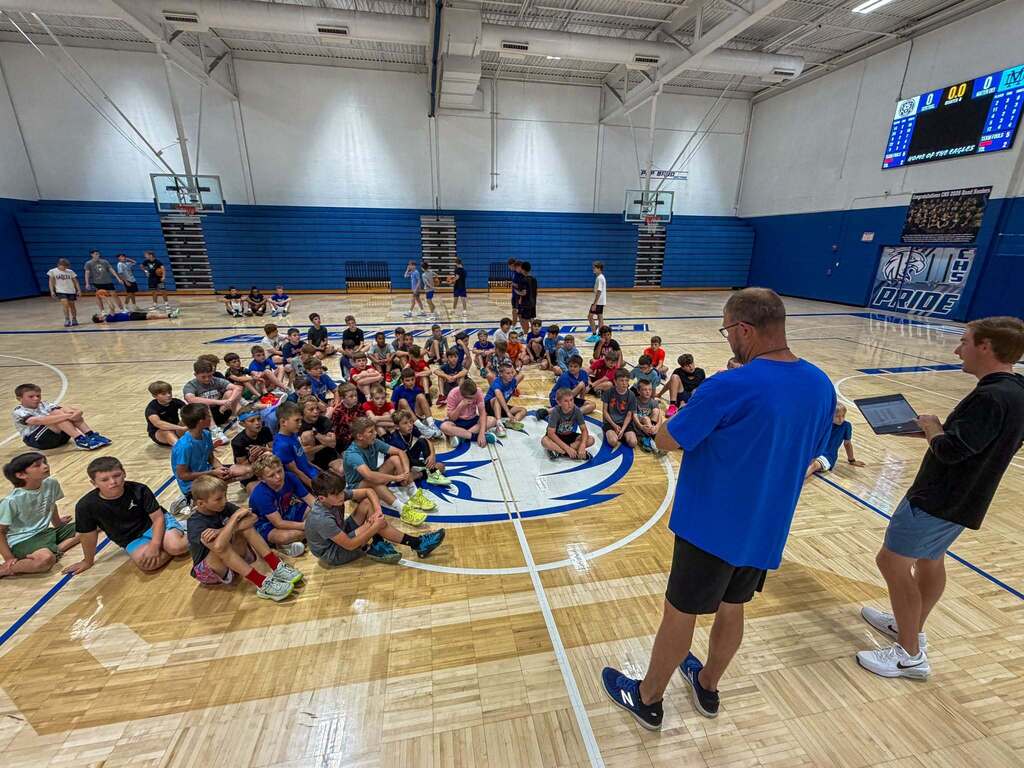 group of kids sitting on gym floor listening to their coach talk