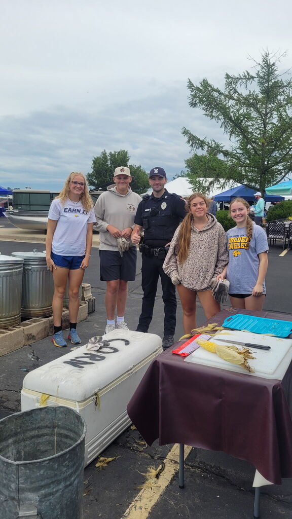 Four students and Officer Keegan ready to serve corn at Lions Club fundraiser.
