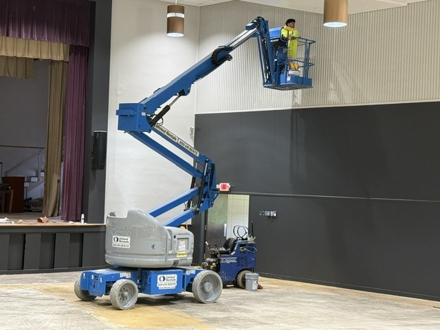 A person on a lift working inside the Cook Elementary School Auditorium. 