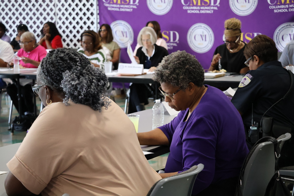 Attendees at the Superintendent's Roundtable take notes, during a presentation, while sitting at a table.