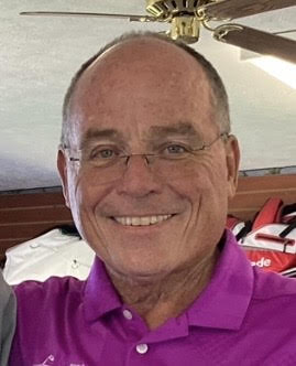 photo of Pete Balerud wearing a magenta polo smiling and wearing glasses. golf shop in the background