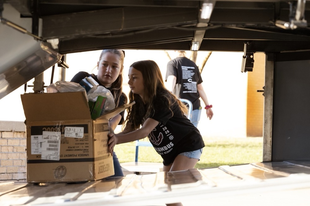 Two members of the CMS Student Council load a box of donations under the CPS touring bus. The group delivered more than 3,300 pounds of food.