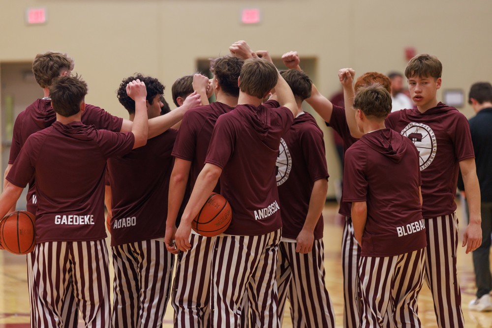 Boys basketball team wearing the traditional maroon and white stripe pants in a hudle