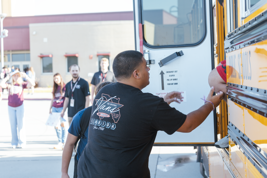 A pair of sophomore students reach to assist an out of frame student who is evacuating a bus during a drill.
