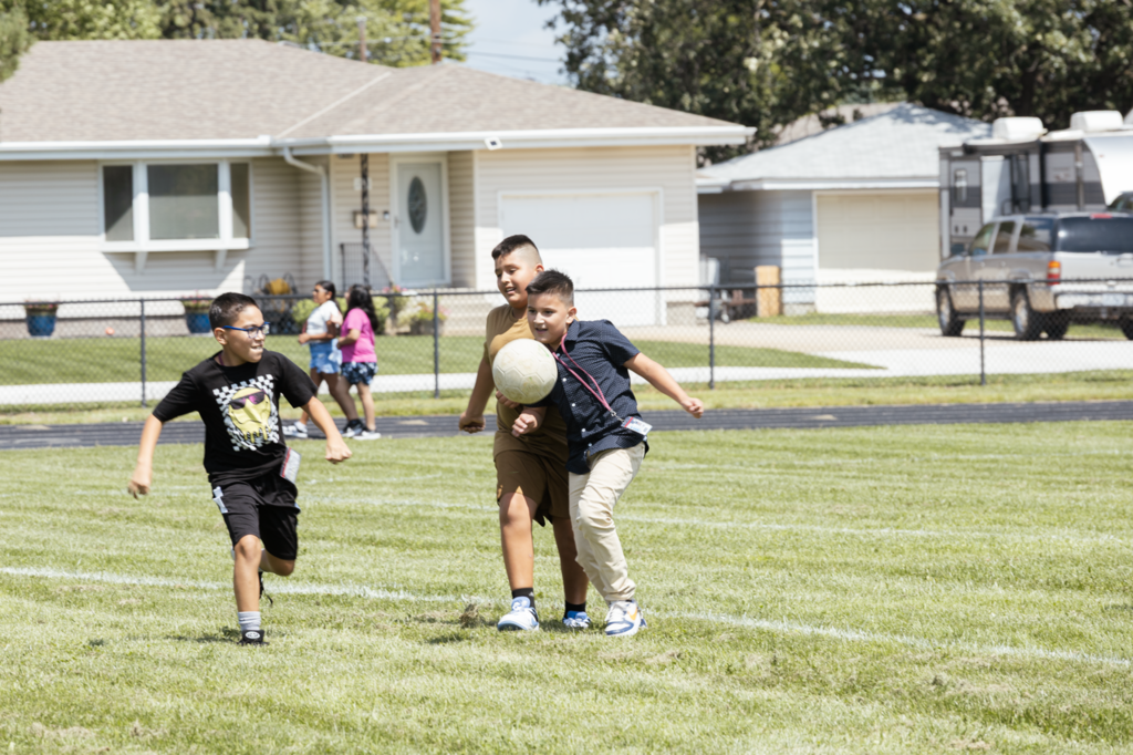 A group of CMS 5th-grader boys play soccer at the football field while two girls walk the track in the background.
