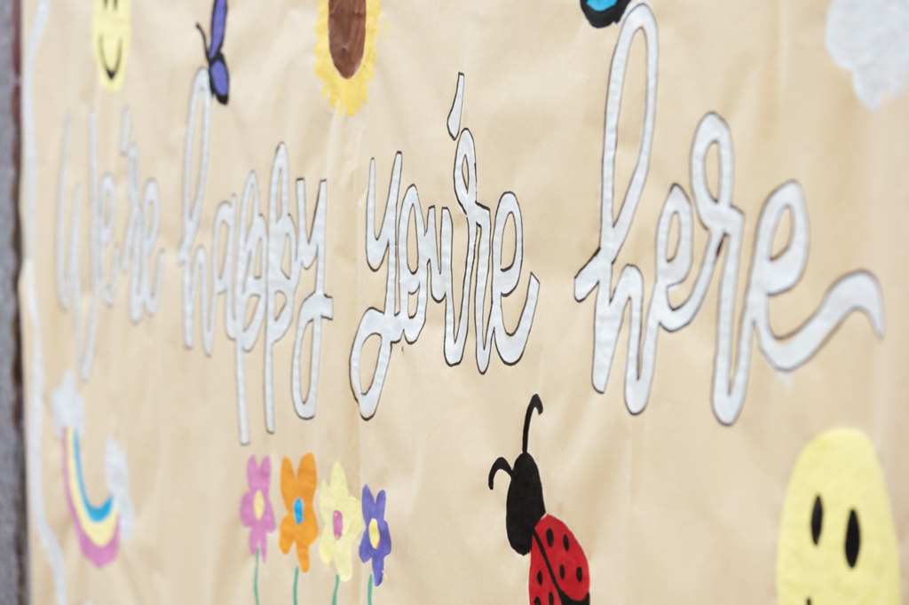 A sign reading "We're happy you're here" in a script writing.