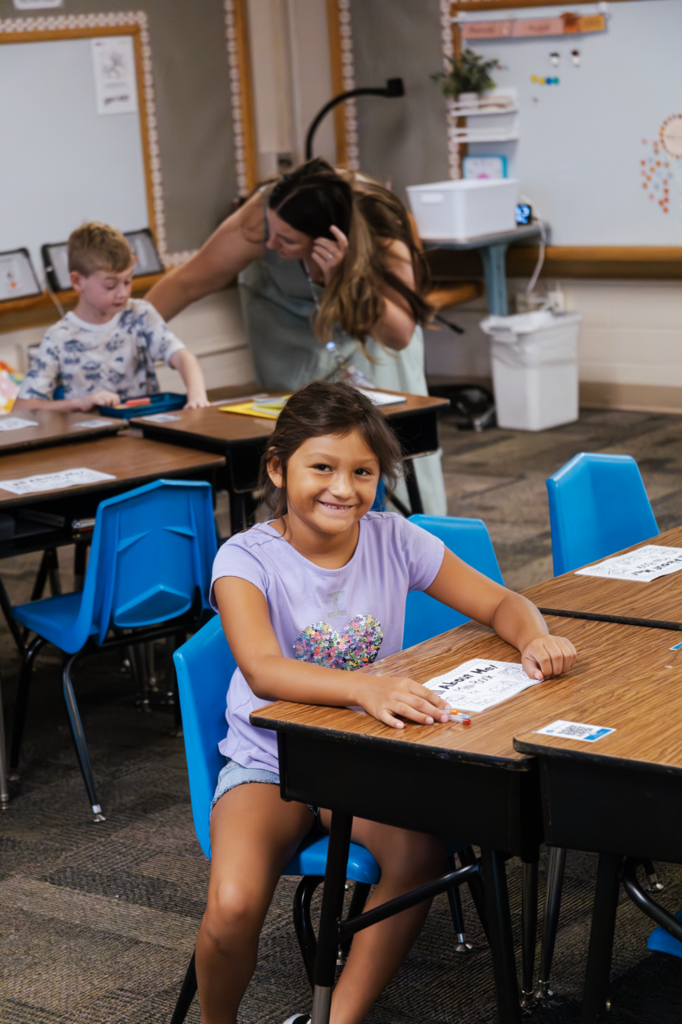 A West Park second grader smiles for a photo while Ms. Grossnicklaus helps a fellow student in the background.