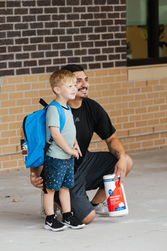 An adult man and preschool student pose for a photo outside of Kramer Preschool during student drop-off. 