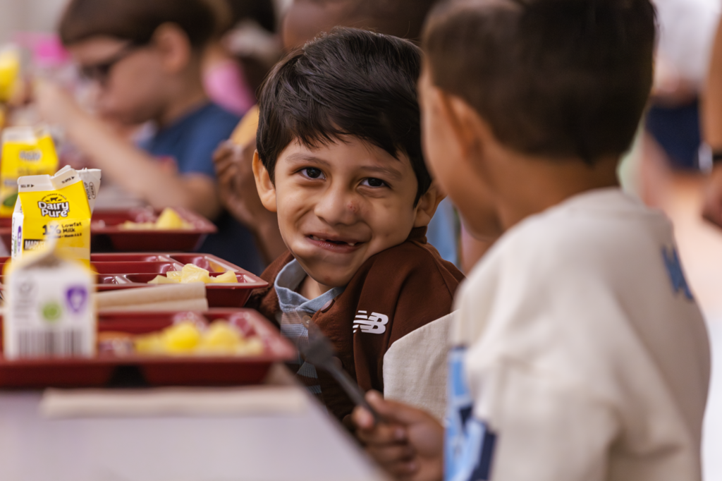 A boy holds a piece of fruit in his mouth as he smiles with a fellow student during breakfast before their first day at Kramer Preschool. 